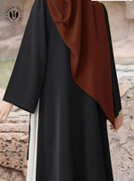 Modern black abaya with side lace-up detail, worn with brown hijab, outdoors in UAE