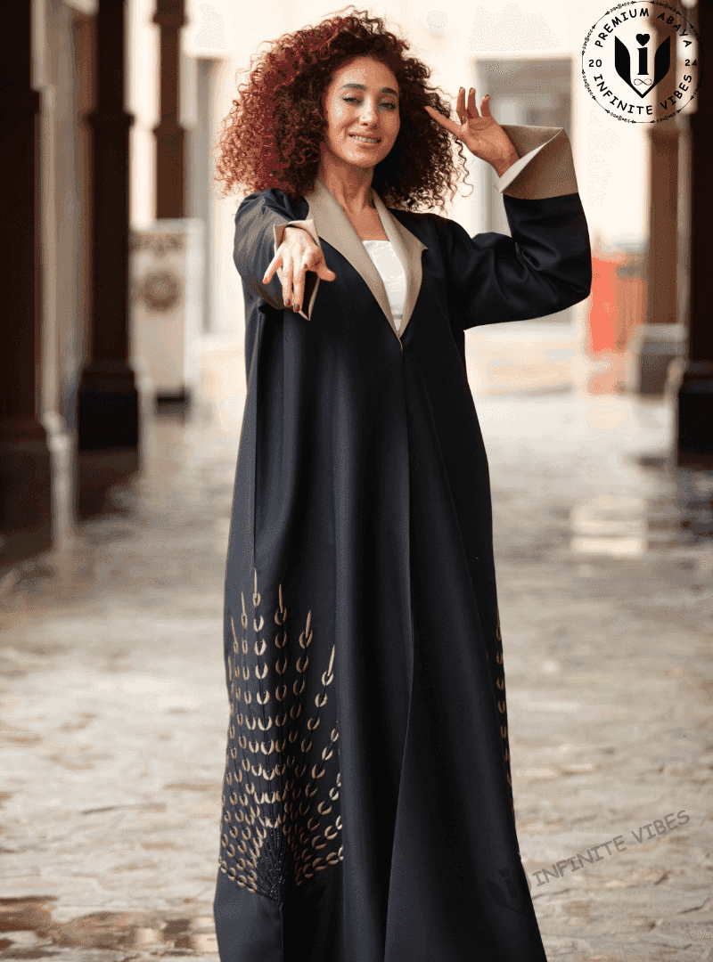 Woman wearing a luxury black abaya with gold embellishments, standing in an outdoor corridor.