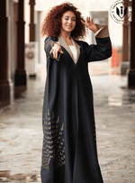 Woman wearing a luxury black abaya with gold embellishments, standing in an outdoor corridor.