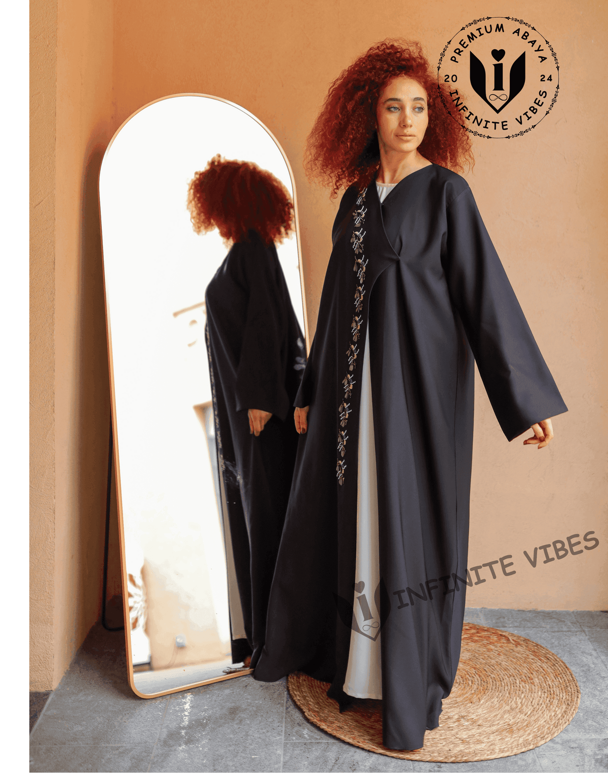 Woman wearing a black designer abaya with embroidery, standing by a mirror indoors.