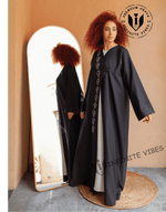 Woman wearing a black designer abaya with embroidery, standing by a mirror indoors.