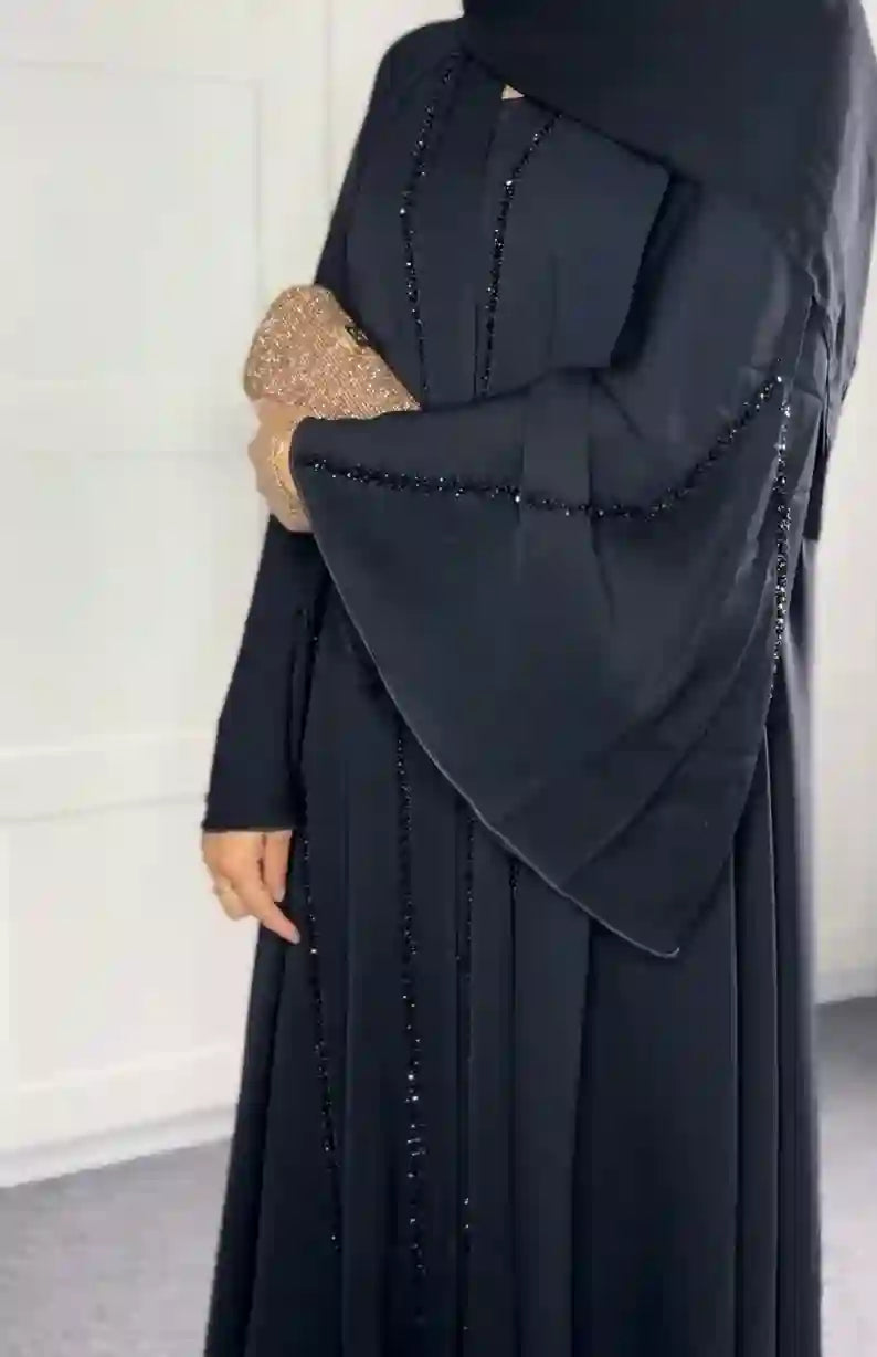 Luxury black handwork abaya with beaded detailing and wide sleeves, woman holding clutch