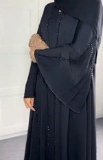 Luxury black handwork abaya with beaded detailing and wide sleeves, woman holding clutch