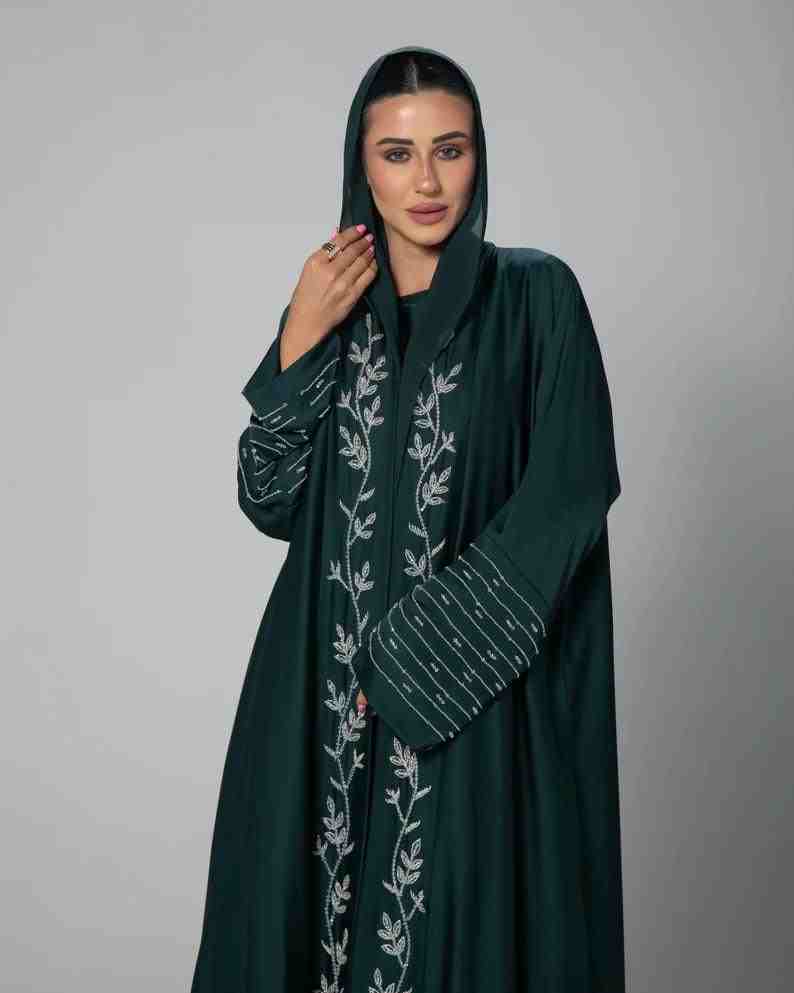 Woman wearing a dark green embroidered abaya with a hood, modest fashion style.