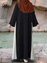 Woman wearing black and white side-tie abaya with brown hijab by rocky water.