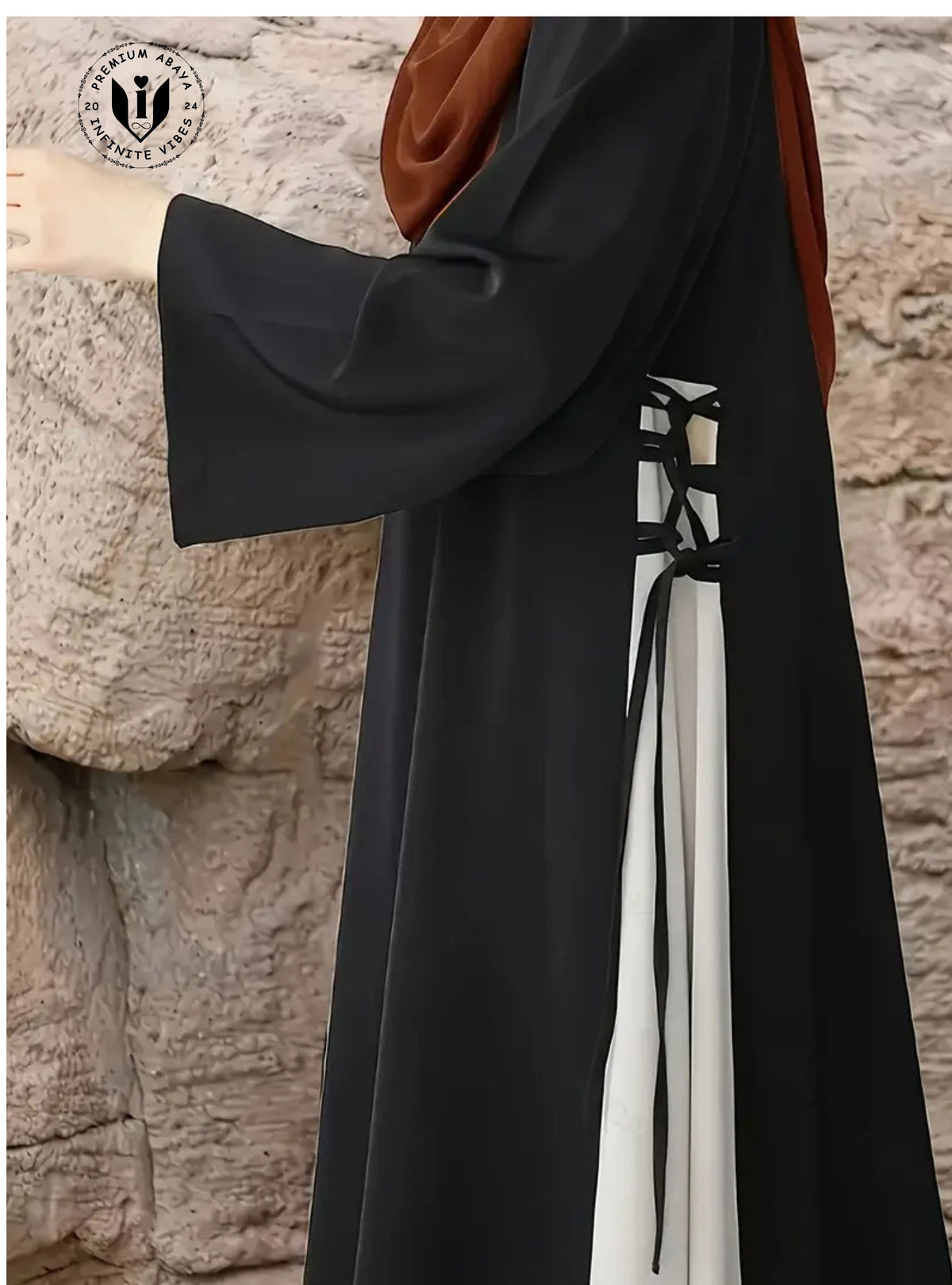 Black abaya with white details against a stone wall background