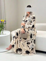 Woman wearing cream floral printed abaya with hijab, holding clutch, seated indoors