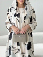 Woman in a floral print designer abaya with hood, holding a beige purse, modest fashion