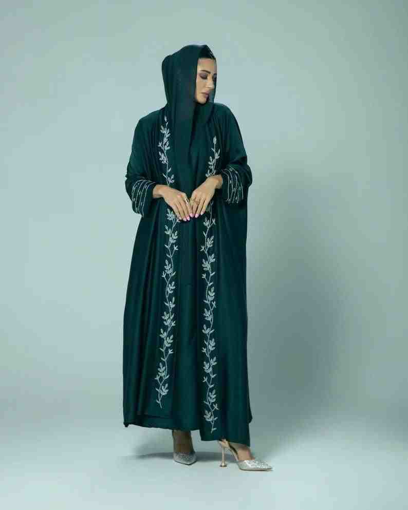 Woman wearing a dark green embroidered abaya with long sleeves and hood, modest fashion