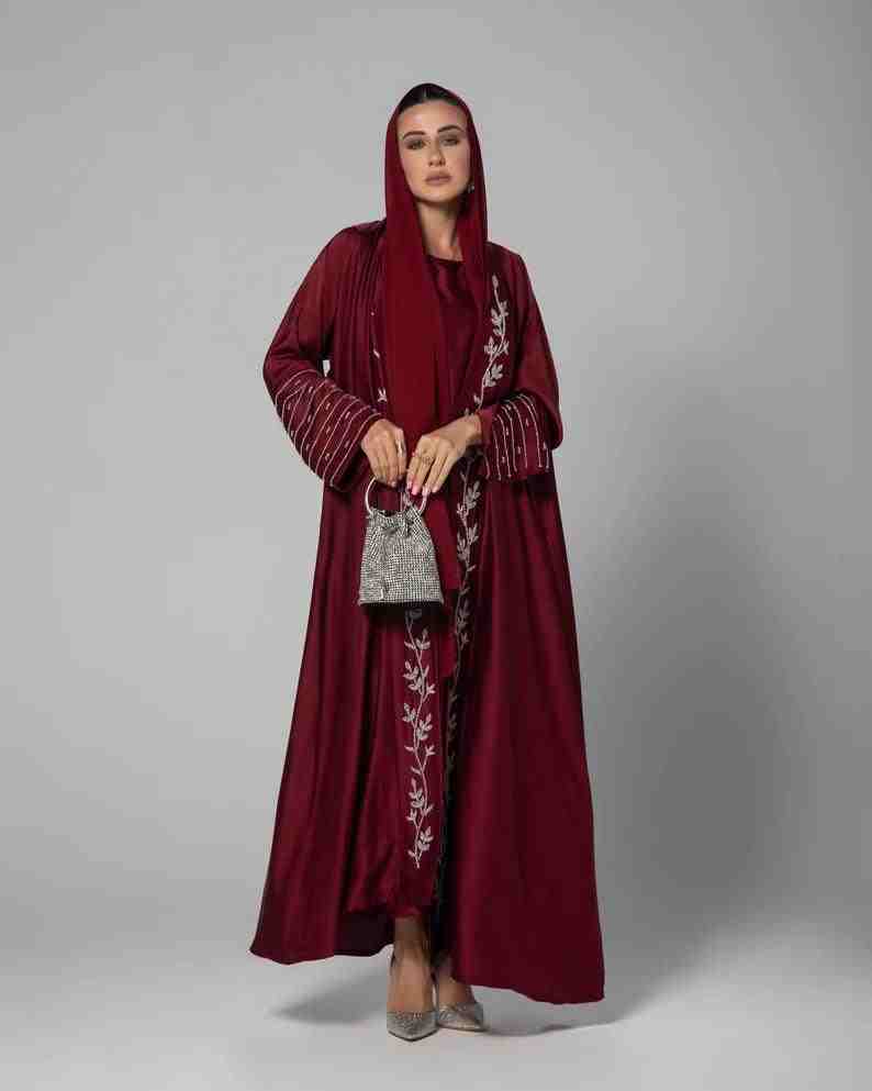 Woman in a maroon luxury abaya with silver embroidery and matching hijab holding a silver bag