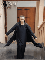 Woman in black designer abaya with gold trim walking on stairs, modest fashion UAE