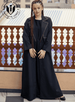 Woman wearing a black designer abaya with contrast stitching on balcony, modest fashion UAE