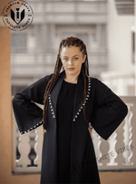 Woman wearing a black designer abaya with white stitched trim, outdoor balcony background