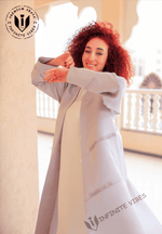 Woman in light grey designer abaya smiling outdoors, showcasing luxury modest fashion.