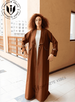 Woman wearing a brown designer abaya with white piping and button details on a balcony