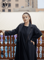Woman wearing a modern black designer abaya with white stitching, standing outdoors.