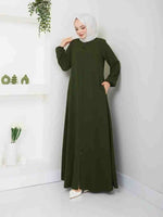 Woman in olive green abaya and white hijab standing indoors, modest fashion