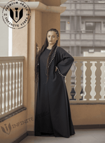 Woman wearing a black designer abaya with scalloped trim, standing on a balcony.