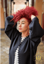 Woman with curly red hair wearing a black embroidered abaya, outdoor setting