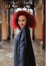 Smiling woman with curly red hair wearing elegant black abaya with detailed embroidery.