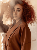 Woman wearing a brown designer abaya with white trim, posing indoors in soft light.