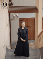 Woman wearing a black designer abaya with gold trim, standing outdoors on stairs