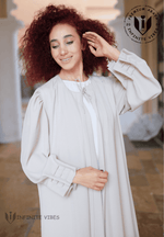 Woman wearing a light beige elegant abaya with pleated sleeves, standing outdoors.