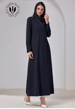 Elegant woman wearing a black buttoned abaya with hood, long sleeves, and white heels.