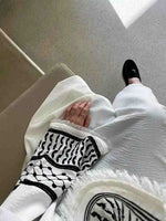 Woman in white open abaya kimono with black embroidery and tassels, black loafer shoes