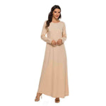 Woman wearing a beige modest abaya dress with long sleeves, standing against a white background