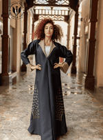 Woman wearing a designer black abaya with gold details in a traditional Middle Eastern corridor