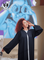 Woman in black handwork abaya posing outdoors with colorful mural background