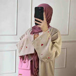 Woman wearing beige heart-embroidered abaya with pink hijab and pink handbag