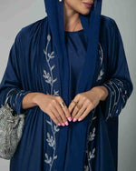 Woman wearing a navy blue embroidered abaya with silver leaf details and holding a sparkly purse