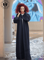 Woman wearing a black designer abaya with long sleeves, standing outdoors on a stone path.