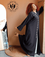 Woman in black embroidered abaya standing joyfully indoors with a mirror reflection