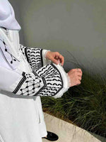 White abaya with black keffiyeh-inspired embroidery and tassel cuffs, worn outdoors