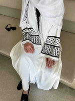 White abaya with black Palestinian embroidery and tassels, worn by seated woman