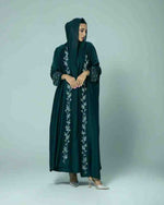 Woman wearing a dark green embroidered abaya with long sleeves and hood, modest fashion